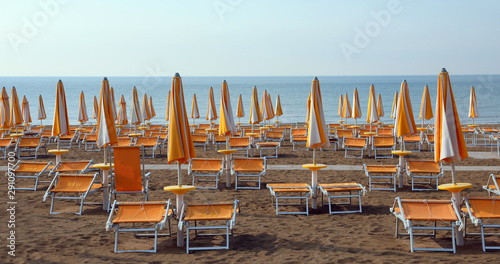 Fototapeta Naklejka Na Ścianę i Meble -  closed umbrellas with deckchairs on the beach without people in