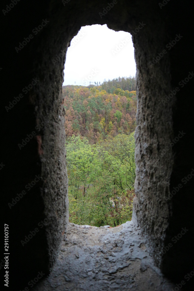 view to the beautiful colorful autumn forest through the window in stone wall of the old castle
