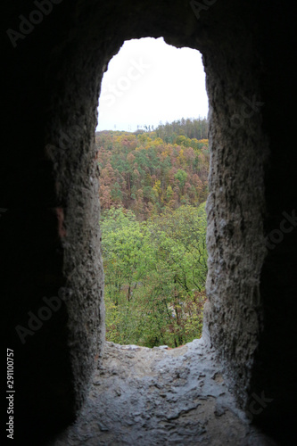 view to the beautiful colorful autumn forest through the window in stone wall of the old castle