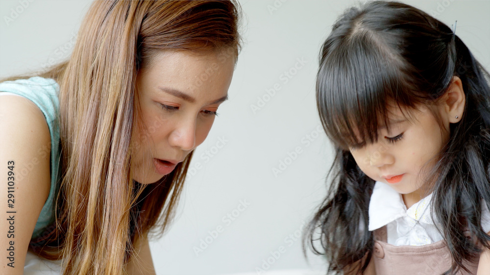 A single mother of Asian ethnic teaching her daughter to draw at home on a beautiful morning sunshine through the large living room window A single mother of Asian ethnic teaching her daughter to draw at home on a beautiful morning sunshine through the large living room window