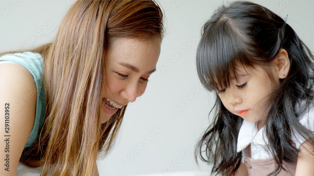 A single mother of Asian ethnic teaching her daughter to draw at home on a beautiful morning sunshine through the large living room window A single mother of Asian ethnic teaching her daughter to draw at home on a beautiful morning sunshine through the large living room window