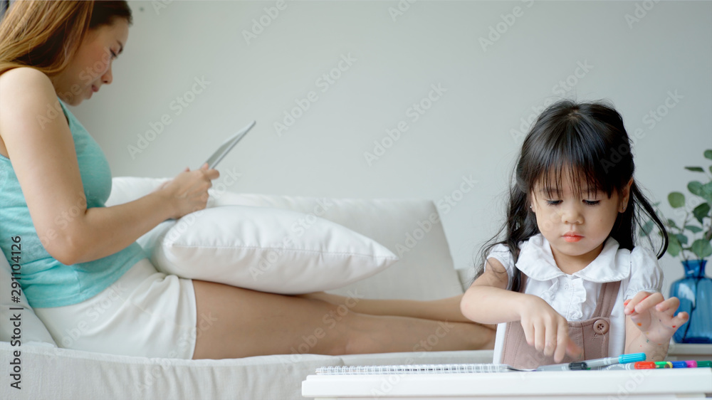 A single mother of Asian ethnic teaching her daughter to draw at home on a beautiful morning sunshine through the large living room window A single mother of Asian ethnic teaching her daughter to draw at home on a beautiful morning sunshine through the large living room window