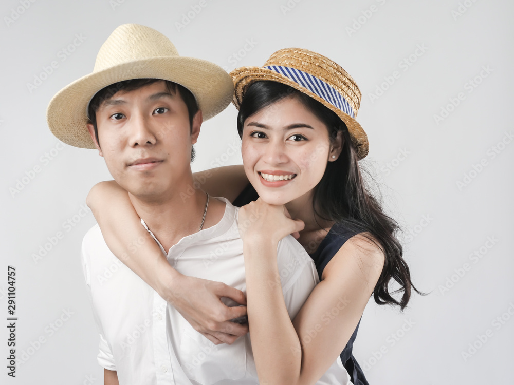 Happy Asian couple wearing hat and ride piggyback on white background.