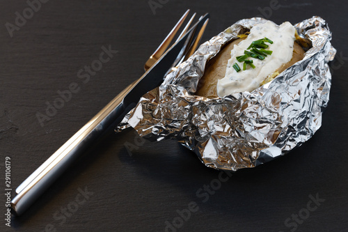 Ofenkartoffel in Aluminiumfolie mit Kräuterquark auf einer Schiefertafel serviert photo