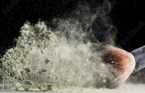 cosmetic brush falls into powder and sprays it on a black background © Vasily Popov