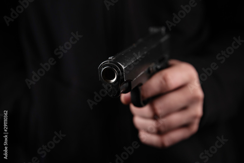 Gun in hand on black background. The threat of a firearm during a robbery on a dark street. Assault with a semiautomatic weapon.