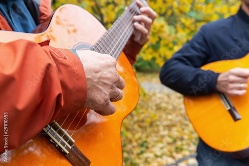 Two friends playing guitars in autumn park