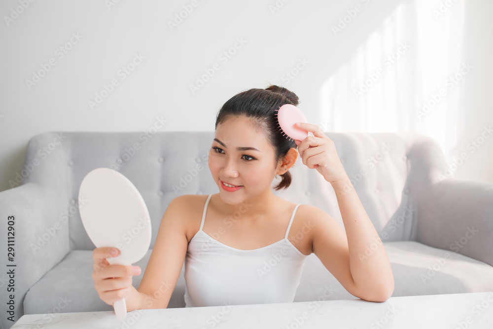 Young Asian woman combing hair and looking in mirror Young Asian woman combing hair and looking in mirror