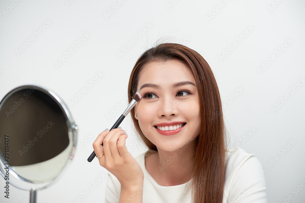 Close up of beautiful face of asian young woman getting make-up. Asian woman is applying eyeshadow on her eyebrow with brush. Beautiful girl look at mirror with hand make. Close up of beautiful face of asian young woman getting make-up. Asian woman is applying eyeshadow on her eyebrow with brush. Beautiful girl look at mirror with hand make.