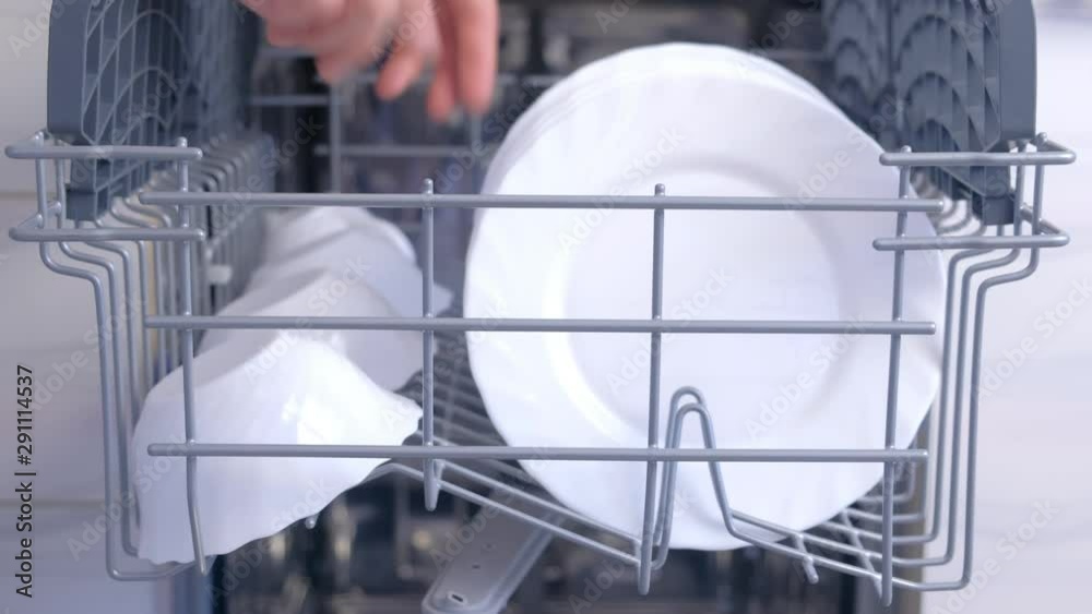 Man taking out white plates and bowls from basket of dishwasher, hands closeup. Getting white utensil and tableware. Washing dishes in kitchen, chores. Household duties using appliances. Man taking out white plates and bowls from basket of dishwasher, hands closeup. Getting white utensil and tableware. Washing dishes in kitchen, chores. Household duties using appliances.