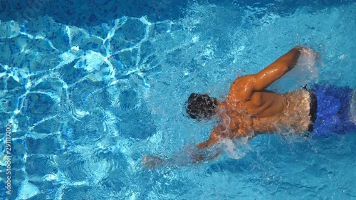 Wallpaper Mural Unrecognizable muscular man swimming in clear blue water of pool. Young sporty guy floating across the basin of hotel on sunny day. Concept of summer vacation or holiday. Top view Close up Torontodigital.ca