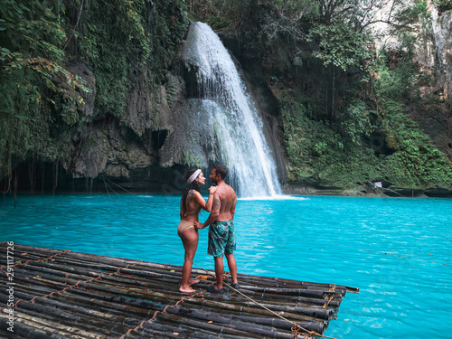 travel couple alone on the bamboo raft in front of the waterfall with turquoise water in Kawasan Falls in Cebu Island, Philippines