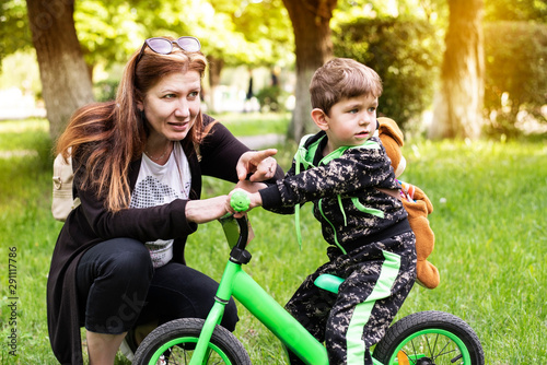 Mom is on good relationship with her little son on a bicycle and walks with him. They have stopped for a rest and mother shows him something and says to be careful on the road