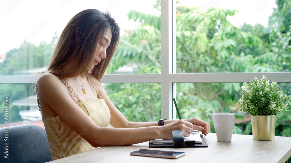 Young beautiful Asian woman enjoying a relaxing moment working and using mobile phone as mobile smart payment to pay for a coffee in the coffeeshop on a bright sunny day Young beautiful Asian woman enjoying a relaxing moment working and using mobile phone as mobile smart payment to pay for a coffee in the coffeeshop on a bright sunny day