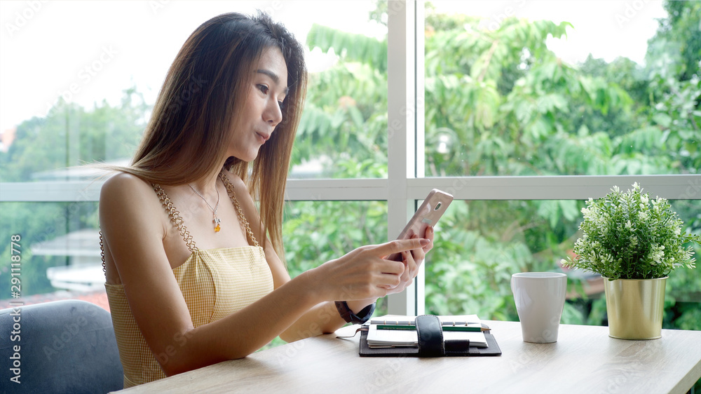 Young beautiful Asian woman enjoying a relaxing moment working and using mobile phone as mobile smart payment to pay for a coffee in the coffeeshop on a bright sunny day Young beautiful Asian woman enjoying a relaxing moment working and using mobile phone as mobile smart payment to pay for a coffee in the coffeeshop on a bright sunny day