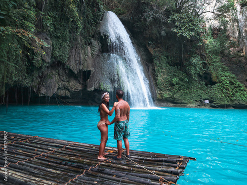 travel couple alone on the bamboo raft in front of the waterfall with turquoise water in Kawasan Falls in Cebu Island, Philippines