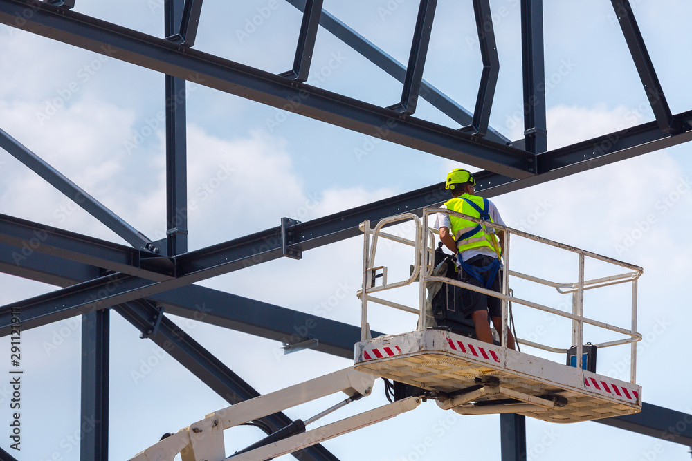 Professional installation work on a construction building site. Assemblers perform high-altitude installation works on the telescopic  boom lifts platforms. Installation of huge steel beams.