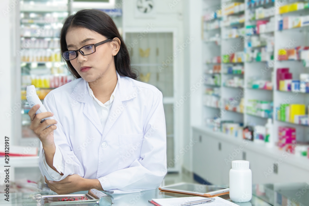 Chemist technician with class dispensing medicine pill on counter with laptop, beautiful Asian pharmacist standing in drugstore doing her work, pharmacist pay attention to the bottle of medicine