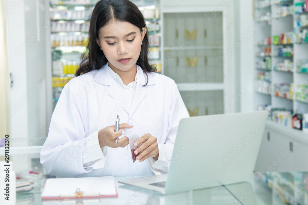 Chemist technician with class dispensing medicine pill on counter with laptop, beautiful Asian pharmacist standing in drugstore doing her work, pharmacist pay attention to the bottle of medicine Chemist technician with class dispensing medicine pill on counter with laptop, beautiful Asian pharmacist standing in drugstore doing her work, pharmacist pay attention to the bottle of medicine