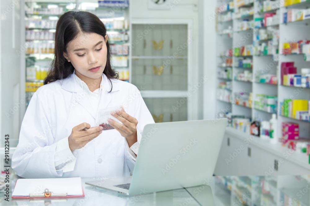 Chemist technician with class dispensing medicine pill on counter with laptop, beautiful Asian pharmacist standing in drugstore doing her work, pharmacist pay attention to the bottle of medicine Chemist technician with class dispensing medicine pill on counter with laptop, beautiful Asian pharmacist standing in drugstore doing her work, pharmacist pay attention to the bottle of medicine