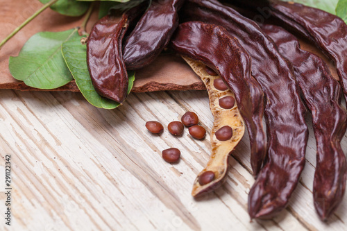 Carob. Organic carob pods with seeds and leaves on white wooden table. Healthy eating, food background.