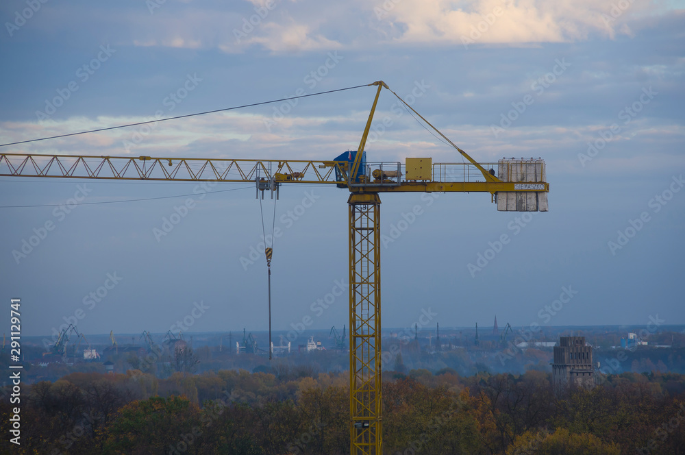 Close-up of yellow crane on a construction site urban landscape technique building construction in the background trees and blue sky port Close-up of yellow crane on a construction site urban landscape technique building construction in the background trees and blue sky port