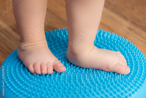 little kid massages his feet while standing on the rug