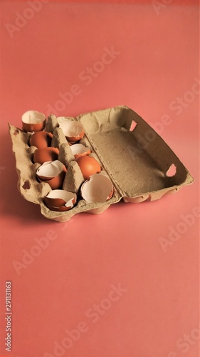 Eggshell halves in recycled cardboard packaging on a pink background. Broken eggs in a craft box, coral-colored surface. Empty shells in cardboard boxes. Processing of food waste, ecology, reuse of