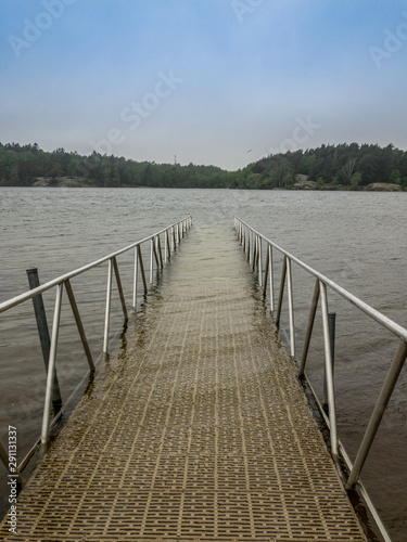 Center front view of a wheelchair ramp and railing leading into cold water in the forest. Blue spring sky