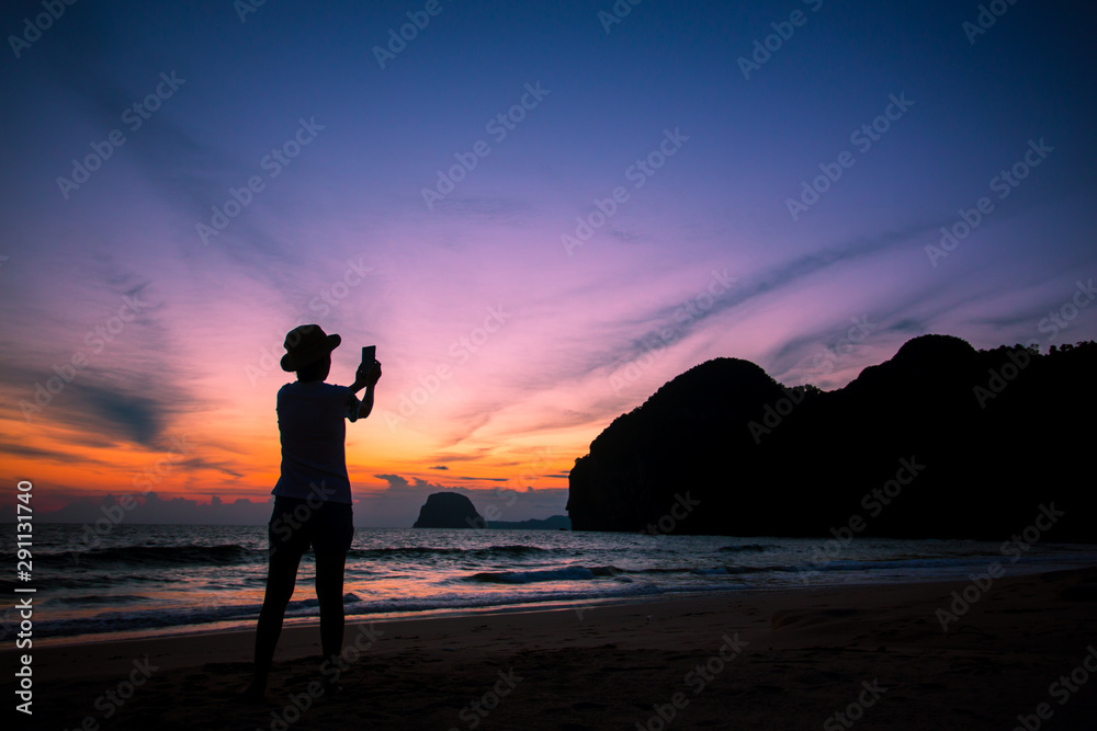Fototapeta premium Silhouette of The girl is walking happily Use the phone at the beach during the sunset and her enjoying freedom feeling happy at sunset 