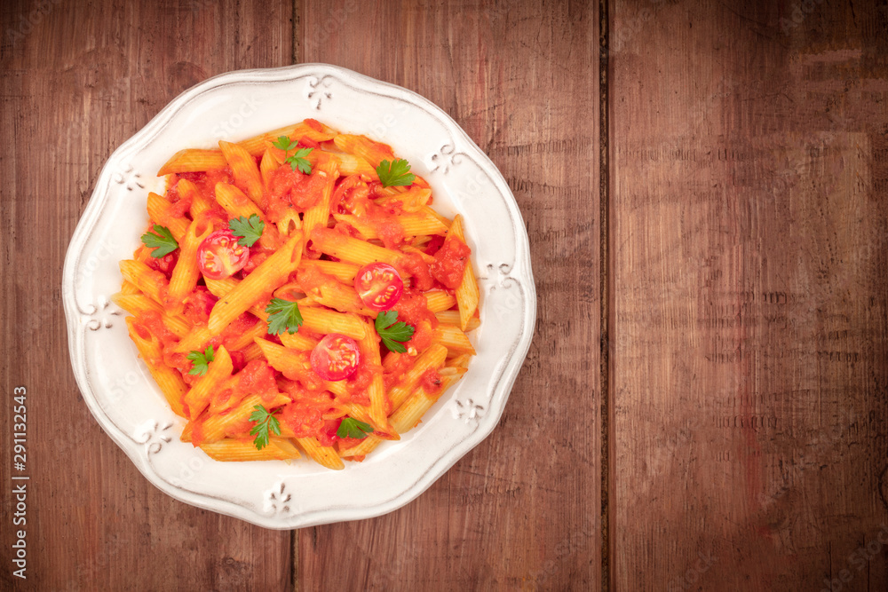 Penne pasta with tomato sauce and parsley, overhead shot on a dark rustic wooden background with copyspace Penne pasta with tomato sauce and parsley, overhead shot on a dark rustic wooden background with copyspace