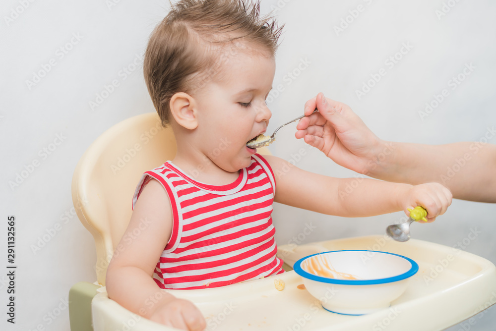 Mom feeds the baby buckwheat porridge in the kitchen Mom feeds the baby buckwheat porridge in the kitchen