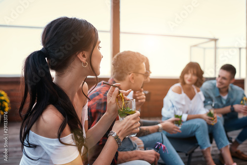 Spending great time together. Young cheerful people chatting and drinking cocktails while sitting on the roof photo