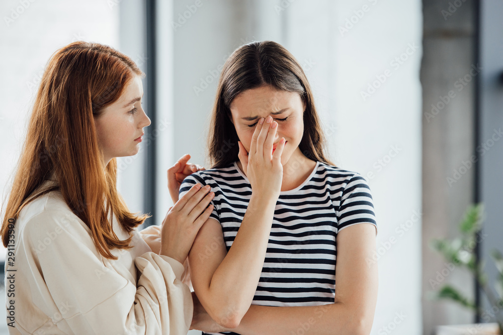 teen girl supporting sad crying friend in striped t-shirt teen girl supporting sad crying friend in striped t-shirt