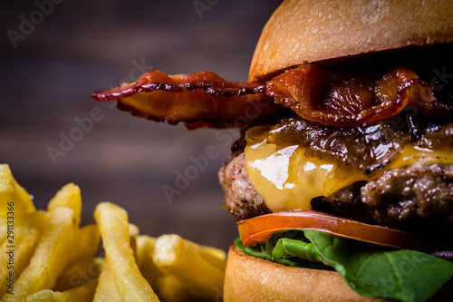 Craft beef burger with cheese, bacon, rocket leafs, caramelize onion and french fries on wood table and rustic background. photo