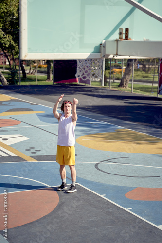 Full-length photo of athlete man throwing ball into basketball hoop on playground.