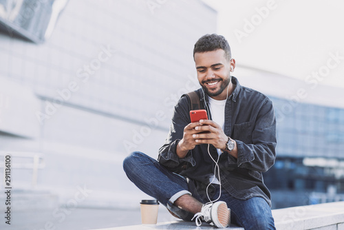 Young handsome men using smartphone in a city. Smiling student man texting on his mobile phone. Coffee break. Modern lifestyle, connection, business concept