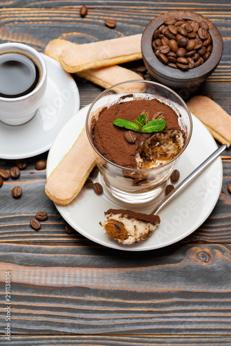 Portion of Classic tiramisu dessert in a glass, cup of coffee and savoiardi cookies on wooden background