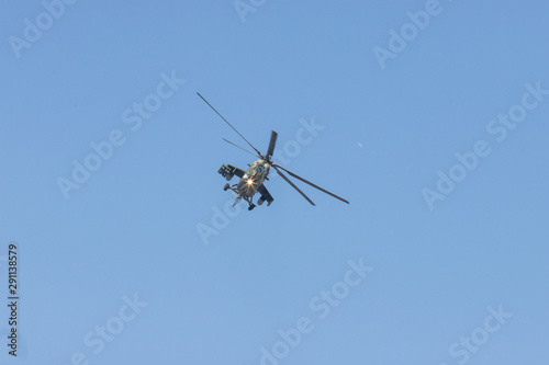 A green military helicopter flying towards the camera - clear blue sky