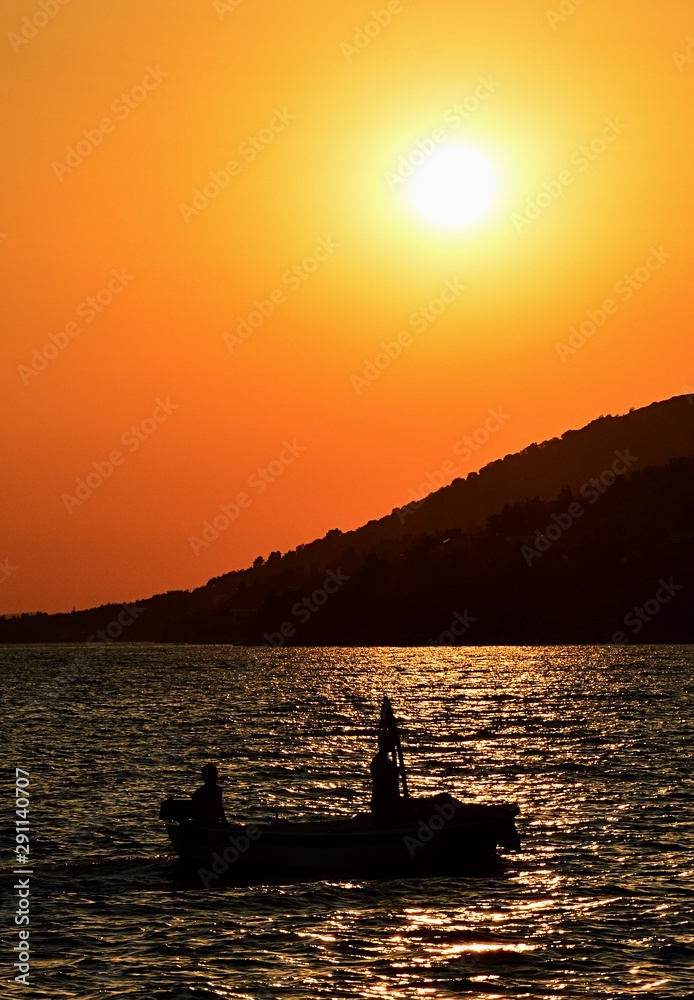 Silhouette of fishing boat and two fisherment during their sunset evening return in Croatian bay near Paklenica national park.