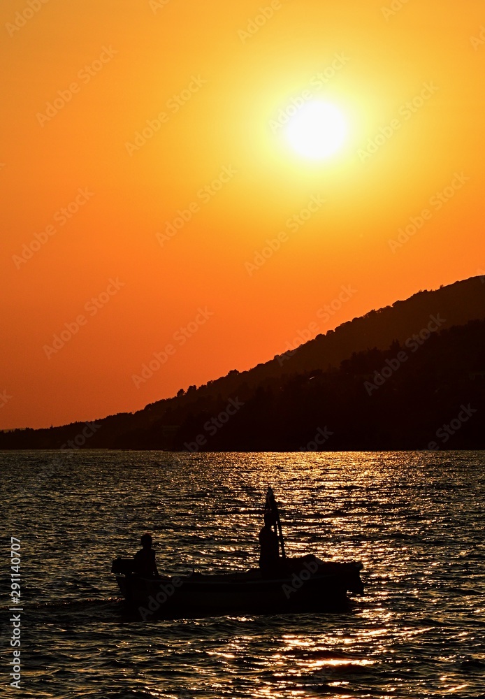 Silhouette of fishing boat and two fisherment during their sunset evening return in Croatian bay near Paklenica national park. Silhouette of fishing boat and two fisherment during their sunset evening return in Croatian bay near Paklenica national park.