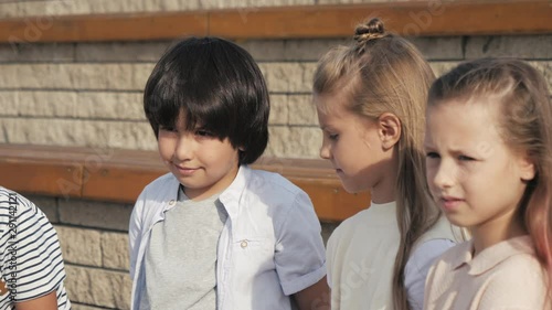 Diverse group of kids sitting on a bench together waiting. photo