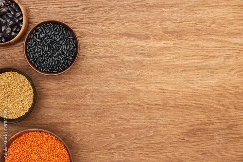 top view of bowls with beans, red lentil, and cereal on wooden surface