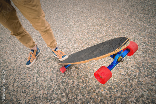 Close-up of male legs in rag sneakers on a longboard on the background of asphalt at sunset. Big skateboard with man legs. Youth leisure concept