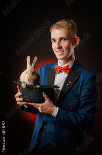 Quadro su tela a young guy magician illusionist holding a hat with a rabbit