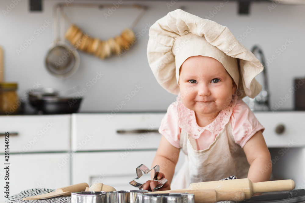 Cute baby cook with wooden tools in a cap and an apron making cookies in the kitchen Cute baby cook with wooden tools in a cap and an apron making cookies in the kitchen