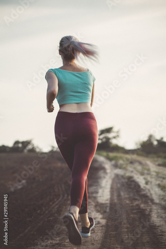 back of young woman in sportswear running distance in the field, girl engaged in sport outdoors, concept healthy lifestyle