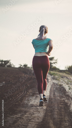 back of young woman in sportswear running distance in the field, girl engaged in sport outdoors, concept active lifestyle