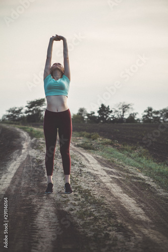 young woman in sportswear exercises and stretches hands up in the field, girl engaged in sport outdoors, concept healthy lifestyle and fitness