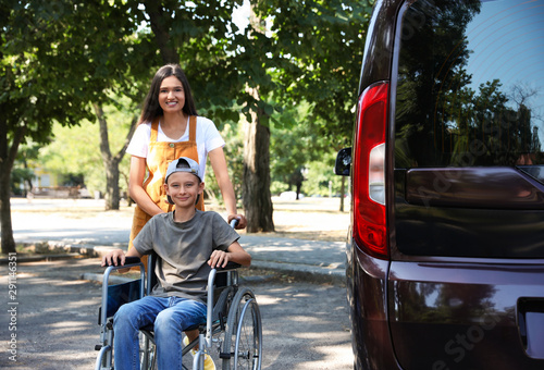 Young woman with boy in wheelchair near van outdoors